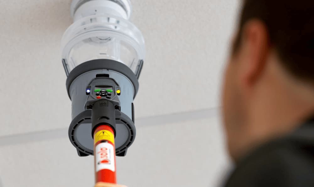 Man holding a Testifire all-in-one detector tester, emphasizing active maintenance of smoke and CO detectors.