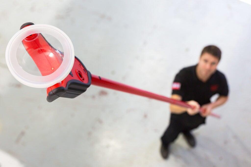 Technician using Solo 365 smoke detector tester on a ceiling-mounted detector.